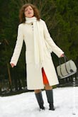 Модное фото девушки в белом пальто в сапогах и с сумкой, стоящей в снегу