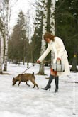 Фото девушки в полный рост в белом пальто с бегущей собакой