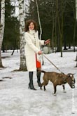 Веселое фото девушки в белом пальто на снегу с убегающей собакой