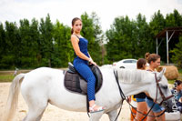 Фото девушки верхом на лошади, вид сбоку, девушка смотрит в кадр
