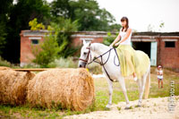Фото девушки верхом на белой лошади рядом с тюками сена, лошадь ест сено