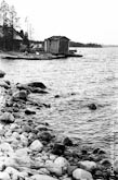 Черно-белый фото пейзаж. Камни на берегу, вдали - деревянный дом