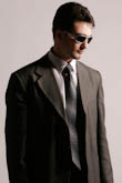 Модный мужской портрет в деловом костюме, галстуке и солнечных очках на сером фоне в студии