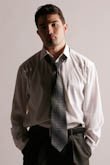 Поясное фото мужчины с руками в карманах в рубашке и галстуке на светлом фоне