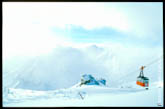 Фото оранжевой кабины фуникулера на фоне светлых, снежных горных склонов Приэльбрусья