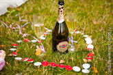 Фото бутылки Мартини и бокалов с шампанским в центре сердца из свечей на траве
