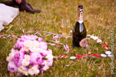 Свадебный фото натюрморт на траве: букет невесты слева, вдали - бутылка шампанского с бокалами