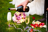 На свадебном фото шампанское наливается в бокалы, стоящие на траве