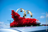 Фото 2-х свадебных колец с колокольчиками на крыше свадебного лимузина с красными розами
