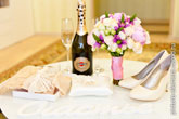 Фото белых свадебных букв «Счастье» на белом столе, чулок, белых туфель и букета невесты, бутылки Мартини с бокалами, обручальных колец на подушке