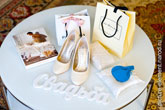 Свадебный натюрморт на белом столе: белые буквы «Свадьба», туфли невесты, коробка с чулками, подарочные пакеты