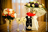 Свадебный фото натюрморт: букет невесты в вазе, свадебные бокалы жениха и невесты, свадебные быки, букет свадебных цветов вдали