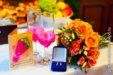 Открытка-приглашение на свадьбу, свадебные бокалы с цветками, коробочка с обручальными кольцами, букет невесты на столе