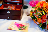 Фото золотых обручальных колец на свадебной декоративной открытке, справа - букет невесты, вдали - деревянная шкатулка с украшениями невесты