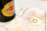 Свадебный фото натюрморт крупным планом: бутылка Мартини слева, справа - обручальные кольца на белой подушечке